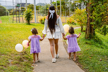 Rear view of Latin family in matching outfits walking through tropical garden with balloons and...