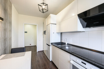 Modern kitchen with white cabinets, black countertops, and wood-look flooring. A geometric light fixture hangs from the ceiling