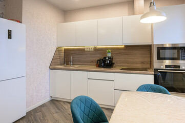 well-lit, modern kitchen featuring white cabinets, wood backsplash, and sleek appliances. Teal chairs complement the light-toned room