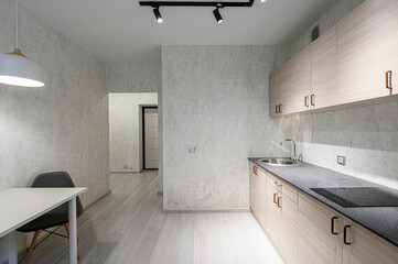 Bright kitchen with light wood cabinets, gray countertops, and a white table with a black chair. Modern lighting and gray walls create a clean, minimalist space