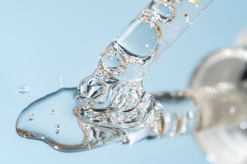 glass pipette dropper close up and Liquid y serum with 24k gold flakes on a blue background. Cosmetics lab research