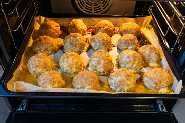 A batch of meatballs baked in the oven on a baking sheet.