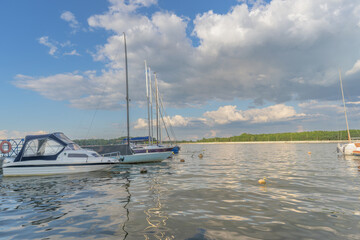 Obraz premium Sailboats docked at quiet marina under clear blue sky. Yachts moored quietly in the harbor, poised for new journeys beneath an endless sky of freedom and possibility.
