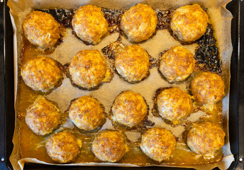 A batch of meatballs baked in the oven on a baking sheet.