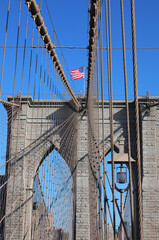 Fototapeta premium New York city with Waving American Flag on the top of Tower of Brooklyn Bridge and steel cables