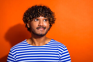 Fototapeta premium Portrait of a young man with curly hair wearing a striped shirt in front of a vibrant orange background