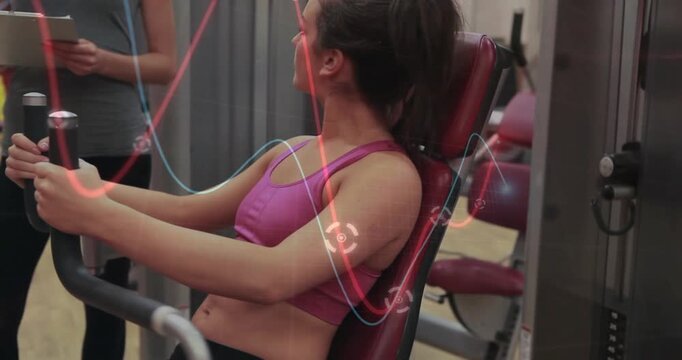 Client gripping chest fly handles starting reps in workout, trainer recording biometric graphs