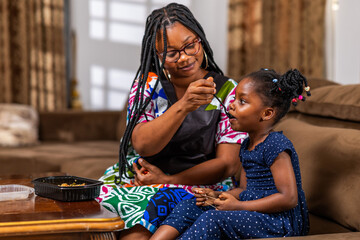 Caring African mother feeding her young daughter at home.