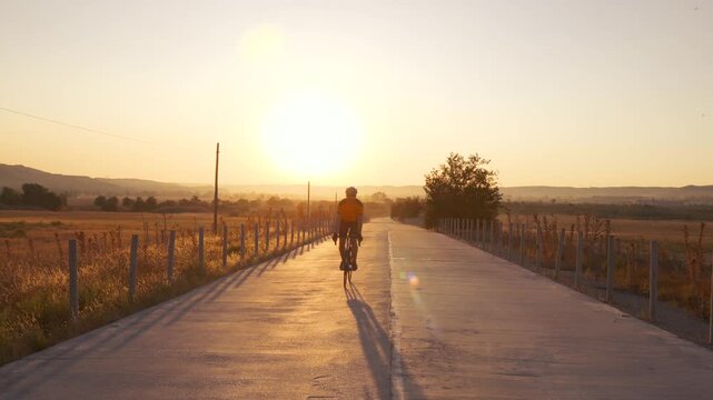 Madrid, Spain. A man cycles slowly past the camera from a distance on a quiet road at sunrise, golden light emphasizing tranquility.