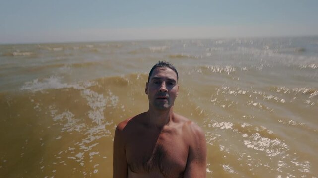 The guy falls backwards into the sea water, standing at a shallow depth. Falling flat into the sea with your back. A man is relaxing by the sea and immersed in salt water.