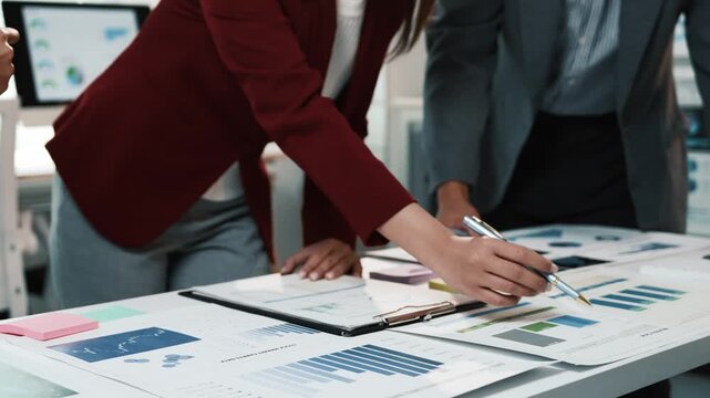 Confident businesswomen reviewing financial graphs, working together on corporate project, sharing insights with collaborative professionalism in modern office setting