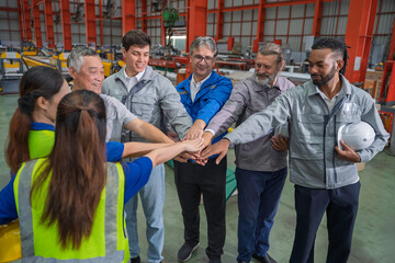Diverse factory workers in safety uniforms joining hands together, showing teamwork, unity, and collaboration in an industrial warehouse environment. Professional work culture.