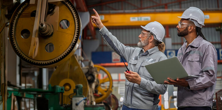 Industrial engineers wearing safety gear inspecting heavy machinery in a modern factory. Factory management, technical maintenance, and engineering teamwork in manufacturing industry. - Powered by Adobe