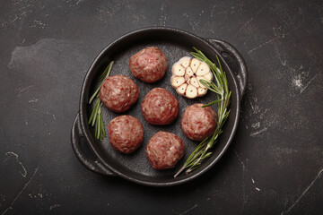 Raw meatballs seasoned with rosemary and garlic are waiting to be cooked in a cast iron pan top view on rustic dark background