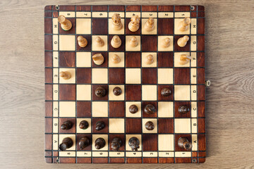 Wooden chessboard with pieces, top view.