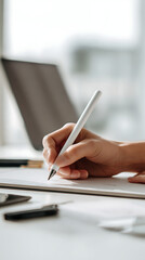 Naklejka premium Hand holding white pen writing on paper with laptop in background notebook