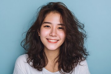 Fototapeta premium A young woman with a joyful expression and voluminous curly hair smiles warmly against a light blue background.