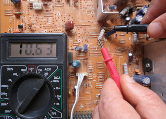 Testing an electronic component with the multimeter. An electrical resistor is testing by a technical staff on circuit board. 