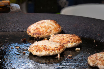 Fresh fish cutlet in a frying pan grill. Barbecue festival in the city park. Street fast food. A large round  grill is roasting fish patties. 