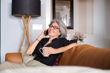 Happy senior woman enjoying a relaxing moment with coffee while chatting on her mobile phone