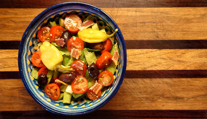 Mediterranean salad of romaine lettuce, cherry peppers, green onion, Kalamata olives, pepperoncini and bacon in an earthenware, hand painted, Talavera bowl on an oak and padauk cutting board  
