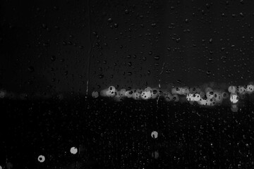 Fototapeta premium Black and white photo of rain drops on a glass window creating abstract texture and moody atmosphere.
