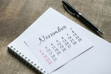 November calendar on blank spiral notebook next to black pen on stone surface. Business, school and academic planning and organization for month of November