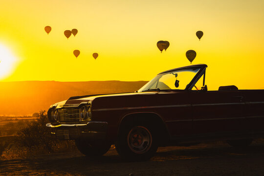 Classic Vintage Convertible Car at Sunrise with Hot Air Balloons in Cappadocia Landscape