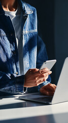 Person wearing denim jacket using smartphone and laptop indoors grey t-shirt mobile phone