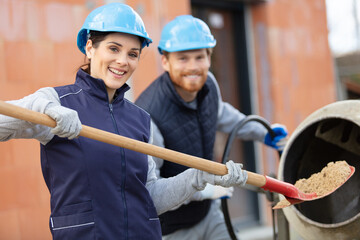 female builder loading sand into cement mixer