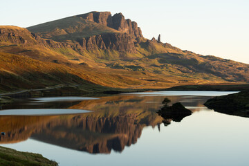 Peaceful morning view of Loch Fada reflecting the dramatic rock formations of the Old Man of Storr on the Isle of Skye, bathed in soft golden light © Philip