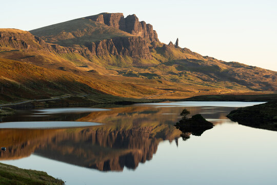 Peaceful morning view of Loch Fada reflecting the dramatic rock formations of the Old Man of Storr on the Isle of Skye, bathed in soft golden light