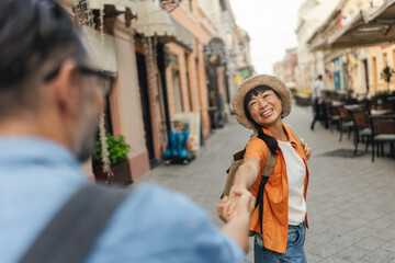 Obraz premium Tourist woman leading her partner by hand while walking through a city street lined with cafes and shops