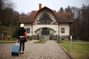 Woman with luggage arriving at a large house.