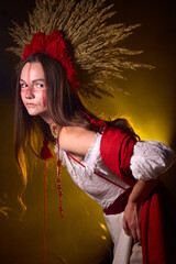 Naklejka premium Mystical woman with striking red face paint and traditional headdress stands against a golden, dramatic background, exuding an air of ancient power and enigmatic beauty .