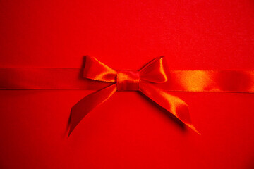 Red satin ribbon with bow on red background, top view