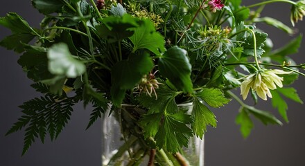 Fototapeta premium Green Bouquet in Glass Vase Fresh Leaves and Pale Flowers on Grey
