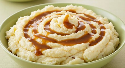 A green bowl filled with mashed potatoes and gravy drizzled in a spiral pattern on top of the potatoes