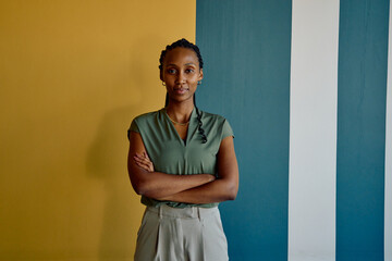 Fototapeta na wymiar Portrait of African young businesswoman standing arms crossed against colorful wall in office
