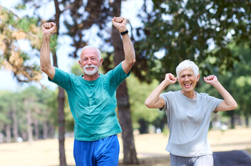 Obraz premium Smiling active senior couple jogging exercising and having fun and giving high five together celebrating victory in the park
