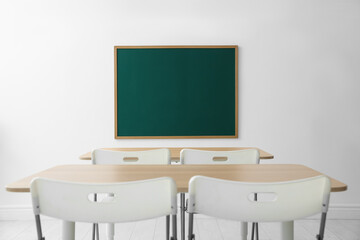 Blank green chalkboard, desks and chairs in classroom