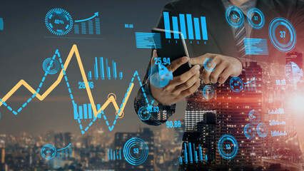 A businessman interacts with a smartphone amid vibrant digital financial charts and data. The city skyline glows at night, showcasing blending technology with urban life. Xenic