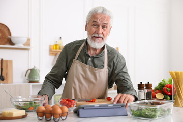 Elderly man using tablet while cooking at white marble table in kitchen