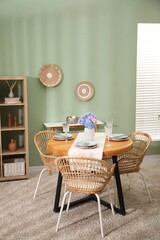 Stylish setting with plates and vase of flowers on wooden table in dining room. Interior design