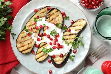 Slices of grilled eggplant with pomegranate seeds and yoghurt on white marble table, flat lay