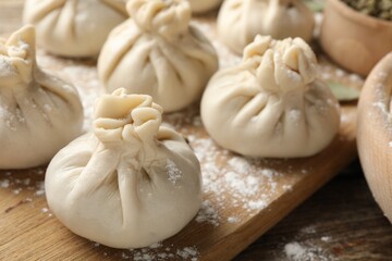 Uncooked khinkalis (dumplings) with flour on wooden table, closeup