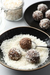 Making tasty chocolate candies with nuts and coconut flakes at white table, closeup