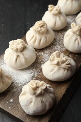 Uncooked khinkalis (dumplings) with flour on black table, closeup