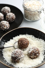 Making tasty chocolate candies with nuts and coconut flakes at white table, closeup