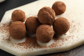 Tasty chocolate candies with cocoa powder on black table, closeup